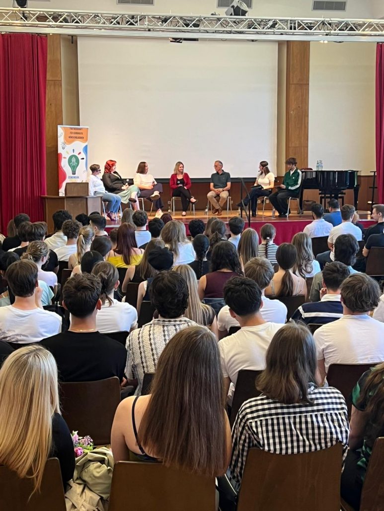 Blick in eine voll besetzte Aula am Gymnasium Odenkirchen: Schülerinnen und Schüler verfolgen eine Podiumsdiskussion zum Thema Verfassung und Grundgesetz auf einer Bühne mit mehreren sitzenden Gesprächsteilnehmenden.